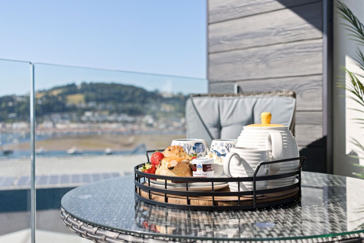 A traditional Devon cream tea served on a tray on a balcony overlooking the river