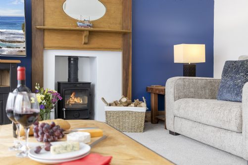 Inviting coastal holiday home lounge with log burner, soft blankets, and a hot drink for a cosy autumn retreat.