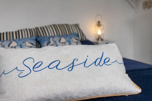 Bright and airy holiday home bedroom featuring a nautical-themed cushion and coastal decor, evoking a fresh seaside feel