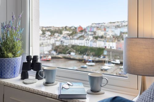 Scenic window seat overlooking the harbour in a holiday home, with binoculars and teacups ready for guests to relax and enjoy the view