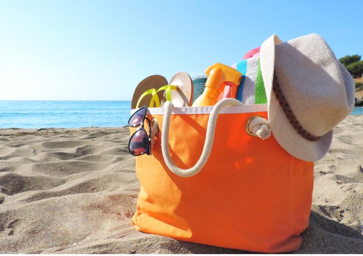 Beach bag packed with summer essentials on a sandy beach