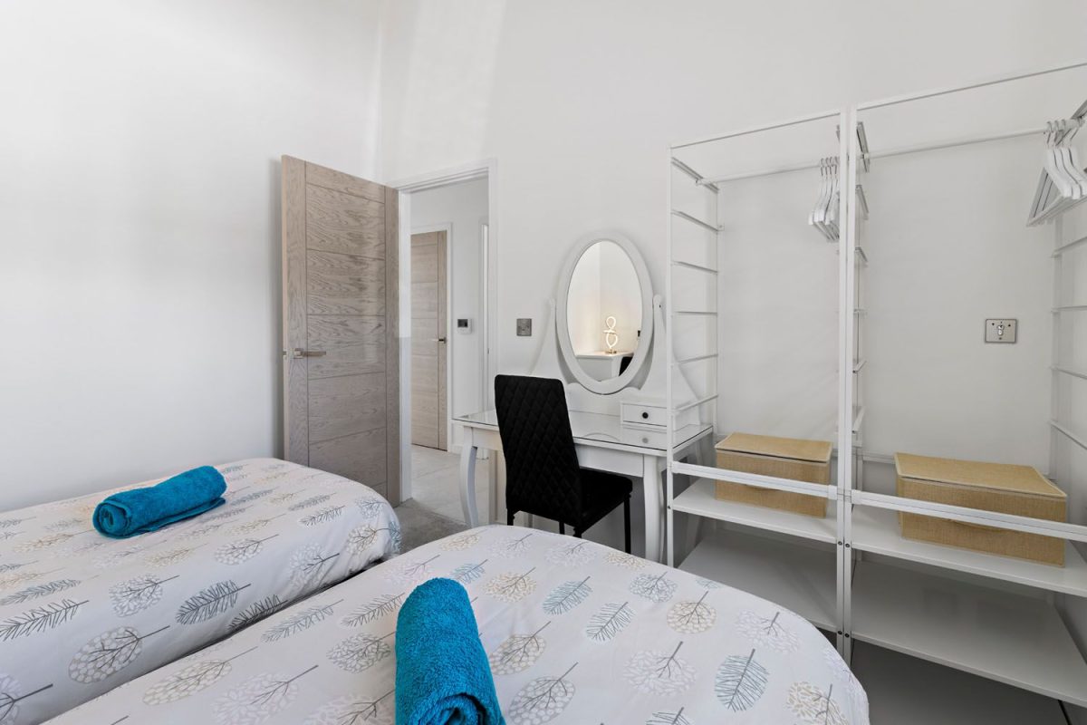 A bedroom in a holiday home in South Devon with freshly laundered towels on the bed, wardrobe storage with hangers and a dressing table with a mirror