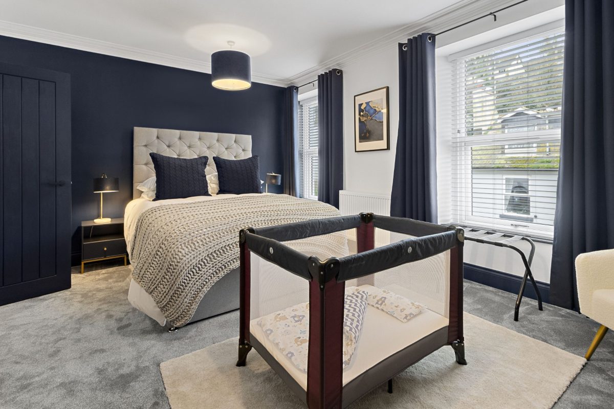 A large bedroom in a holiday home in South Devon with a double bed and an infant's travel cot at the foot of the bed