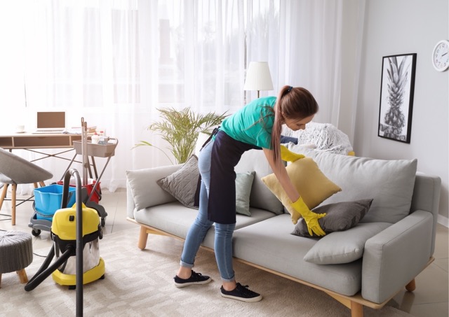 Cleaner arranging cushions on a sofa after deep cleaning a holiday let living room.