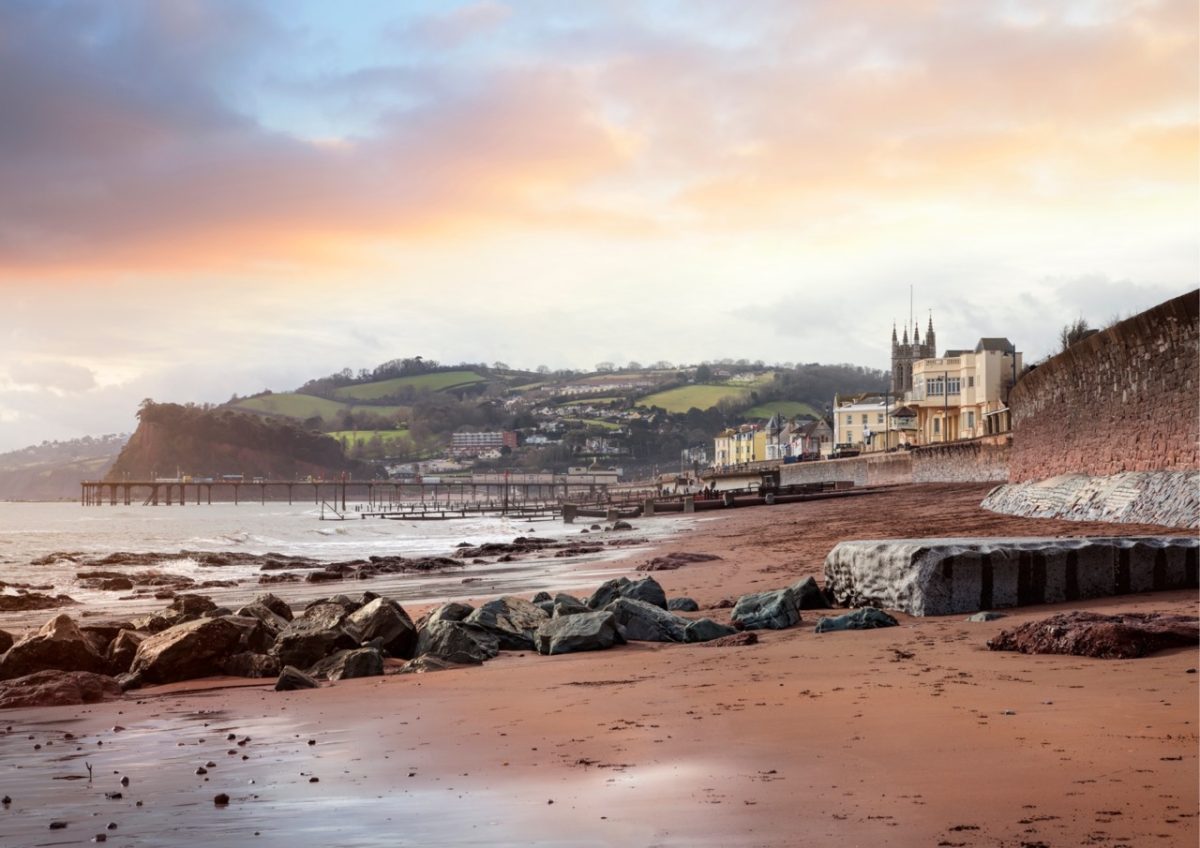 Teignmouth beach in South Devon under a soft, hazy winter sky, with gentle waves washing onto the shore.